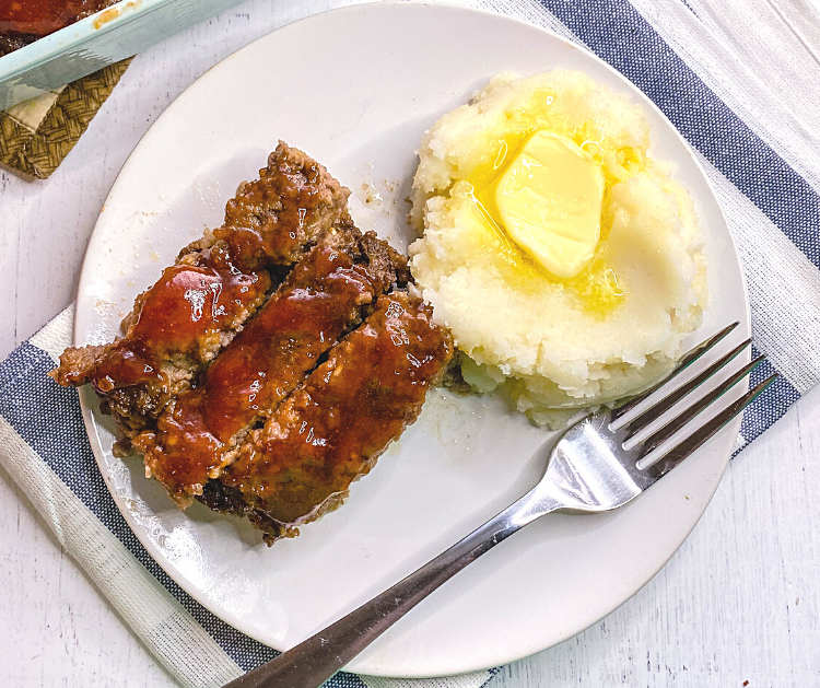 Three slices of meatloaf and a scoop of mashed potatoes with melted butter on a white plate.
