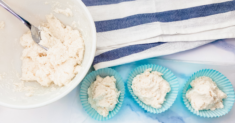 The bowl of biscuit mix and three blue cupcake liners filled with biscuit dough. 