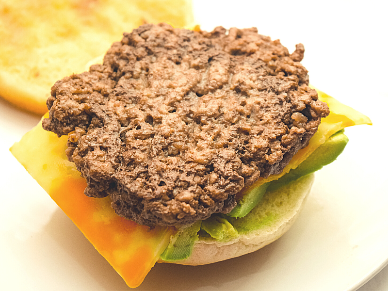 Open faced hamburger with the patty on top, with cheese and fresh avocado. 