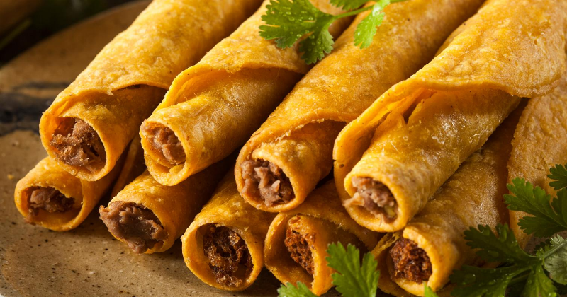 A plate full of beef taquitos with cilantro. 