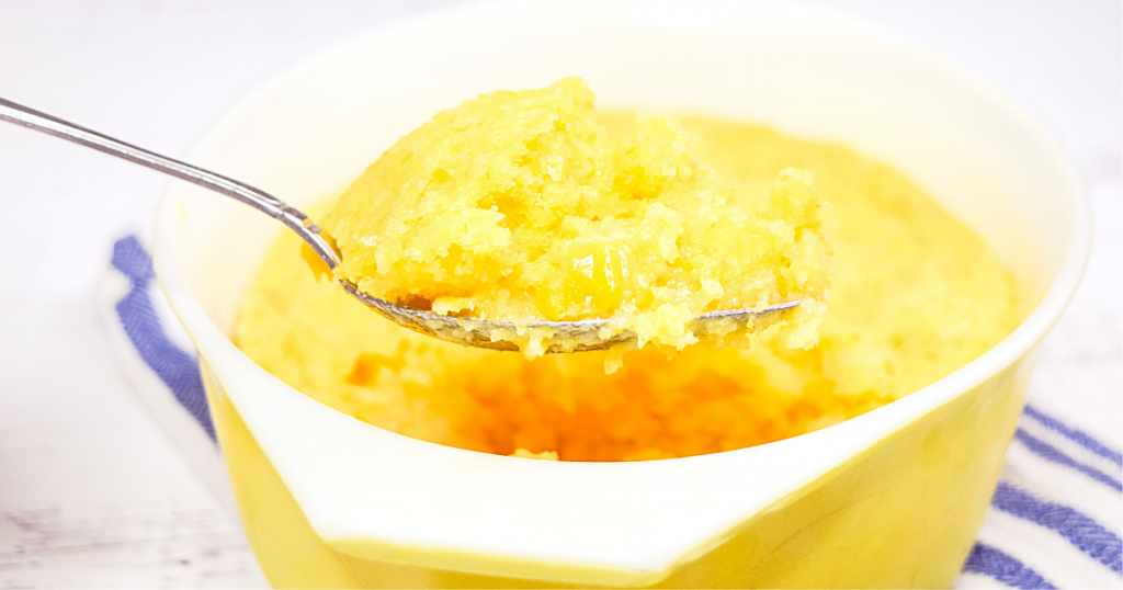 A dish of spoon bread with a big spoonful of it raised up above the dish.
