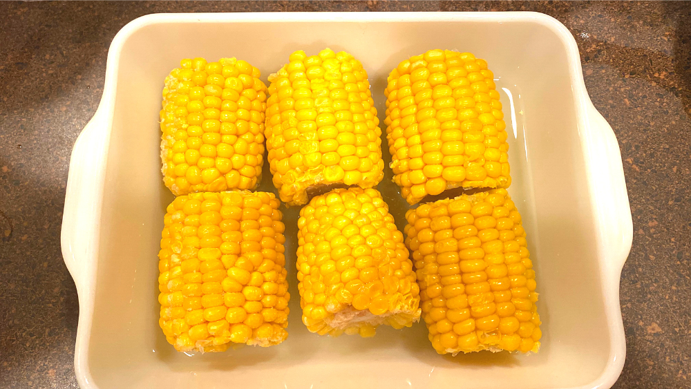 Frozen mini corn on the cobs in a white microwave-safe dish