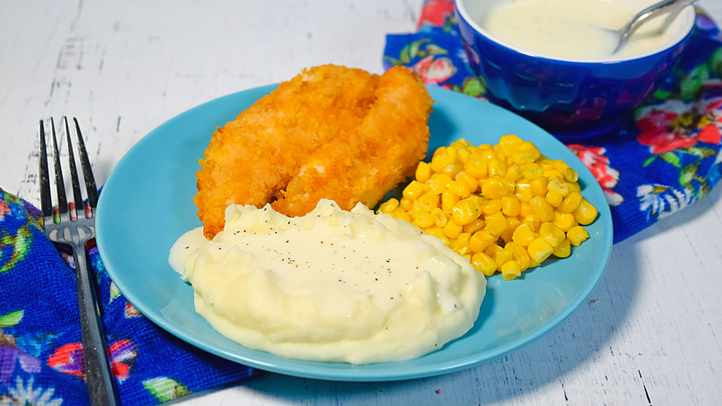 A cornflake chicken meal with mashed potatoes topped with microwave white gravy, cornflake chicken, and corn. 