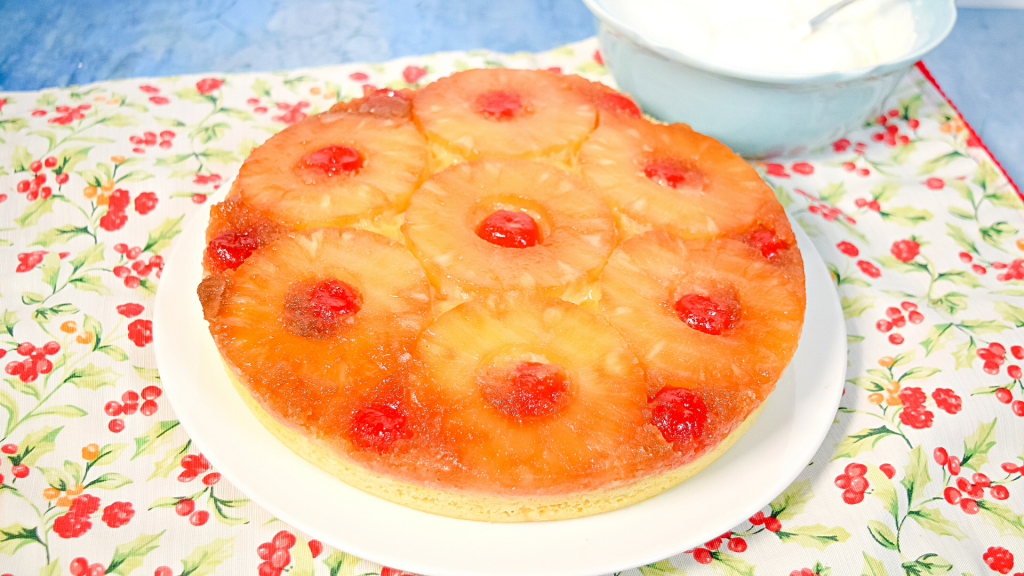 A round pineapple upside down cake on a white and red floral placemat