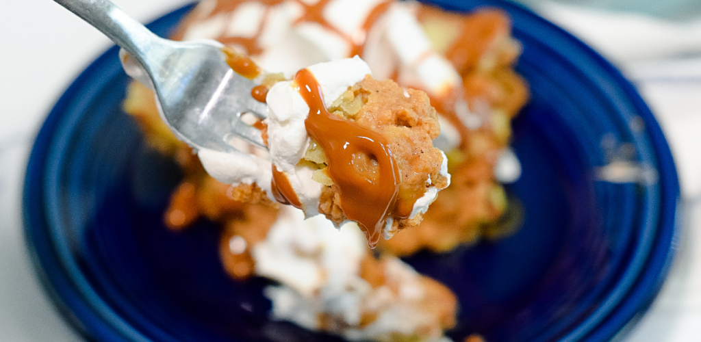 A close up view of a bite of upside down pumpkin pie with Cool Whip and dulce de leche sauce over a dark blue plate. 
