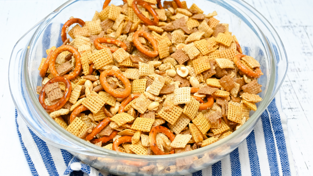 Microwave Chex Mix in a clear glass bowl mixed up with seasoning on a blue striped towel