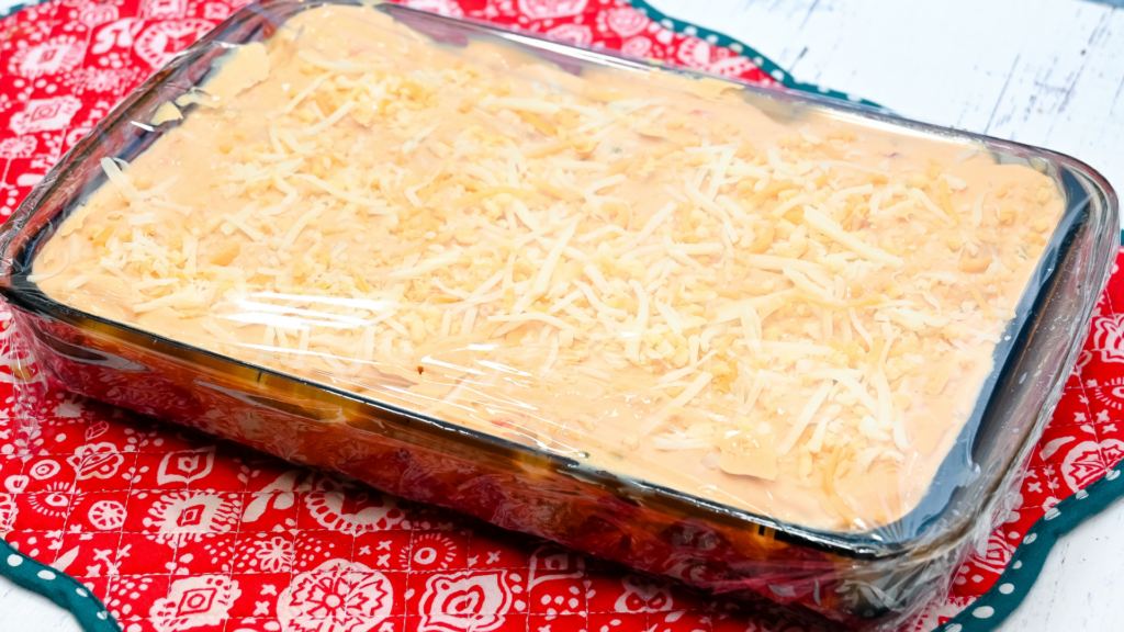 The finished smothered burrito casserole in plastic wrap before cooking in the microwave.