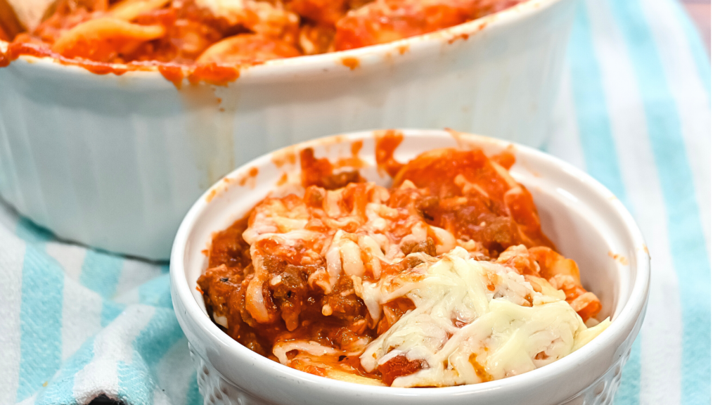 Close up of a bowl of Microwave Cheesy Ravioli Lasagna with Meat Sauce on a pastel turquoise striped towel. 