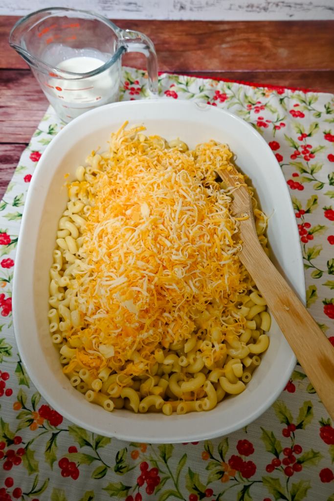 Adding cheese to the macaroni in a white casserole dish.