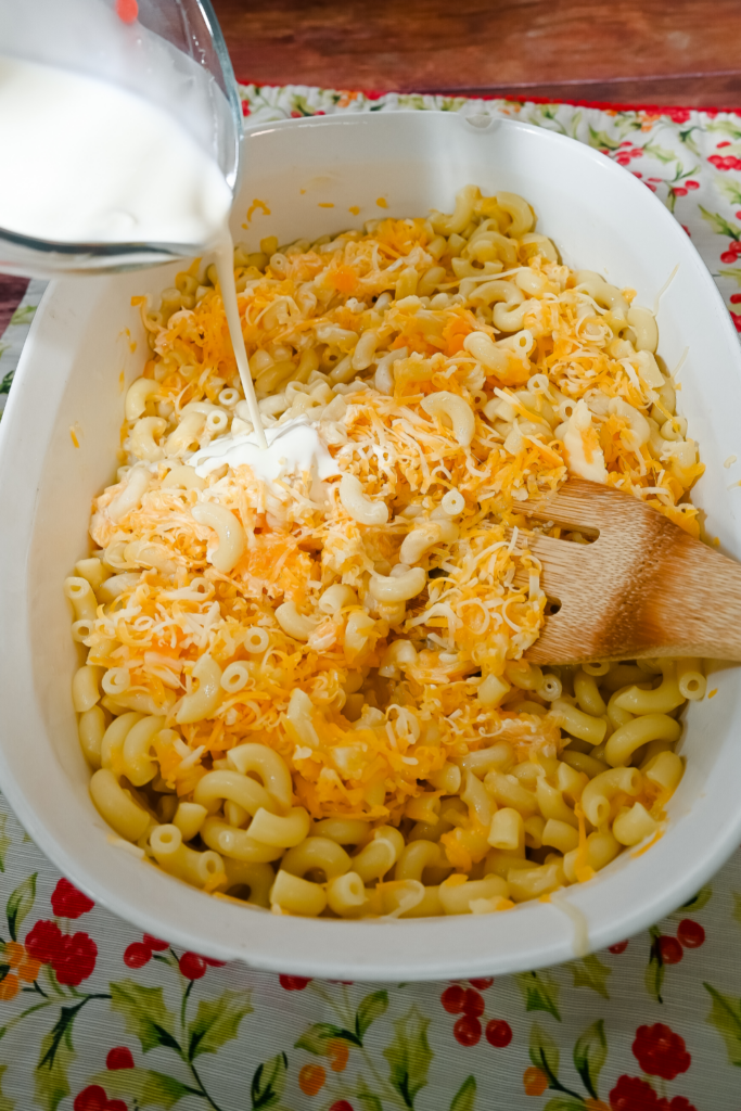 White Casserole Dish adding whipping cream and cheese to the elbow pasta for macaroni and cheese. 