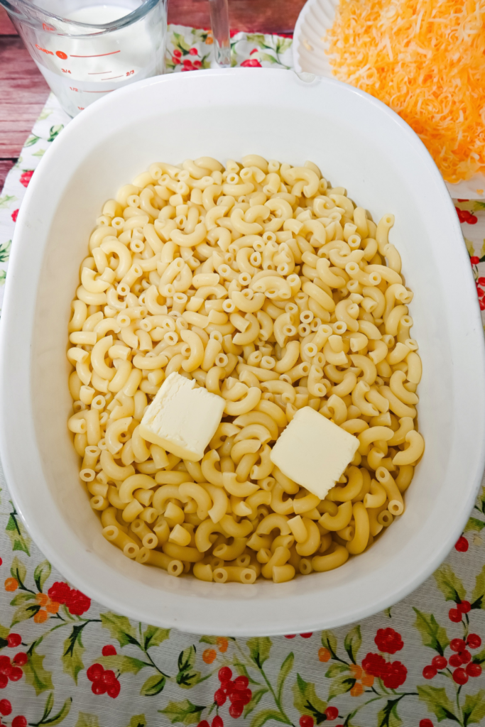 Adding butter to the macaroni in a white casserole dish.