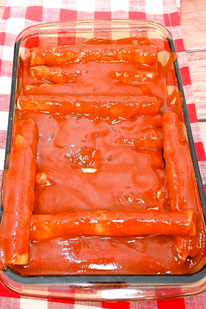 A brown glass 9 x 11 pan with taquitos covered in red enchilada sauce. 