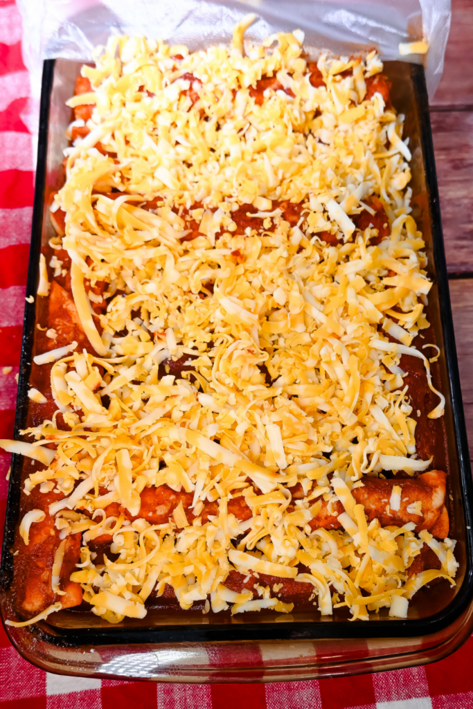 Brown glass casserole dish with overnight enchiladas covered in colby jack cheese. 