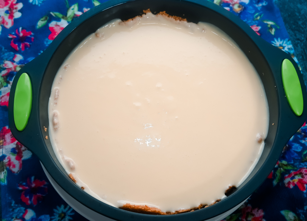 A plain cheesecake in the silicone pan with a plate underneath it ready to go in the microwave