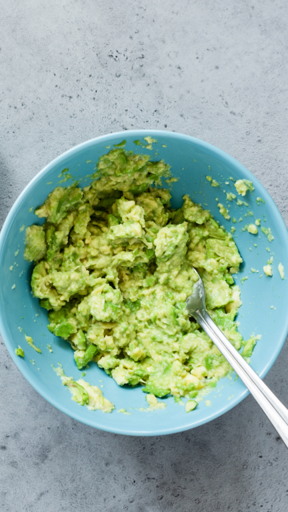 Mashed avocado in a light blue bowl on a gray background.