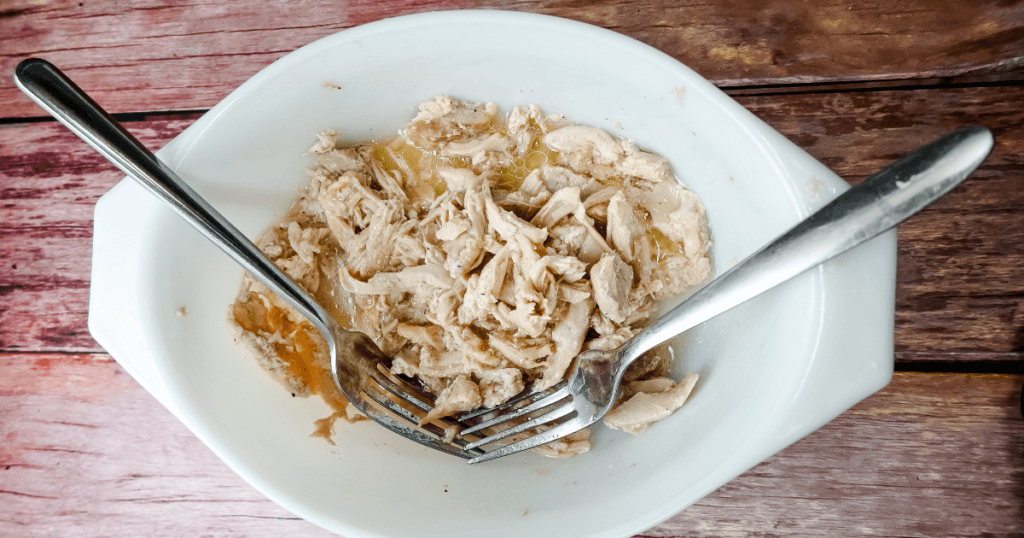 Chicken thighs shredded with two forks in a white bowl on a wooden background