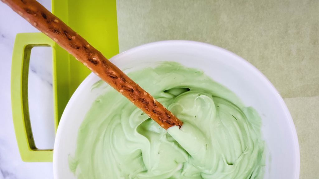 Dipping a pretzel rod into the green candy melts. 