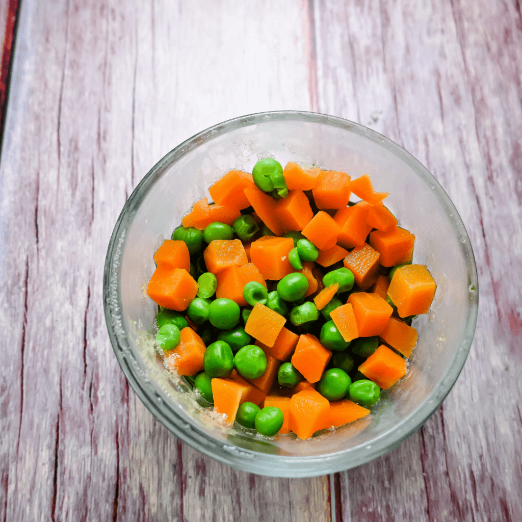 A glass bowl with peas and carrots