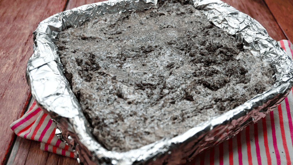 An 8 x 8 pan covered in foil with the OREO marshmallow batter just transferred into it. 