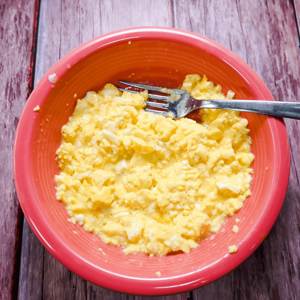 Scrambled eggs with a fork in a salmon colored bowl on a wooden background