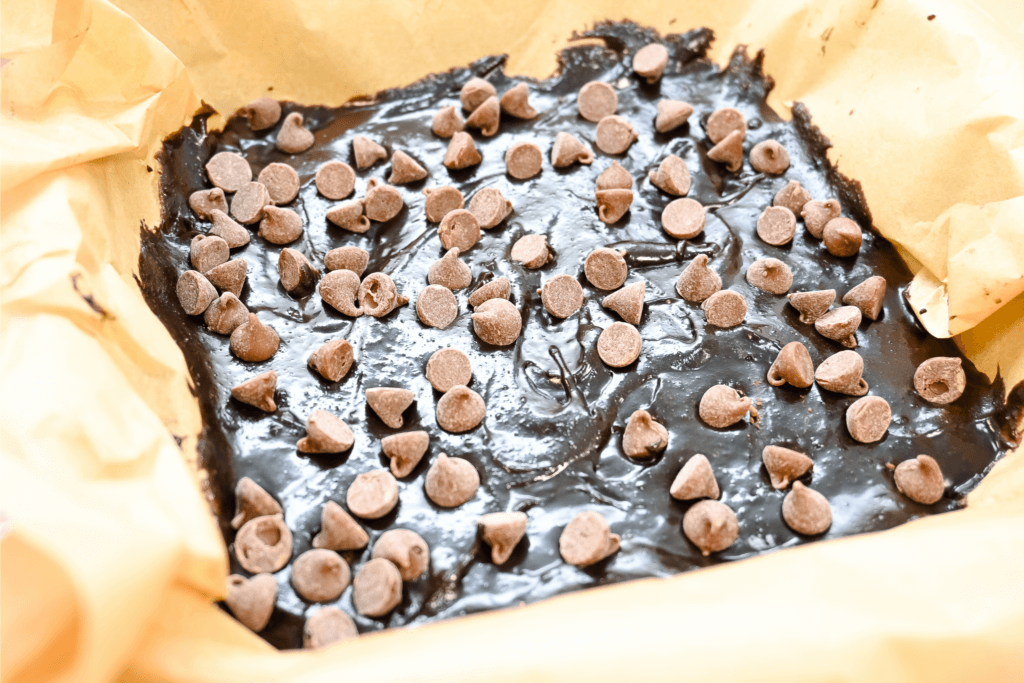 Chocolate chips on top of the brownie batter over parchment paper. 