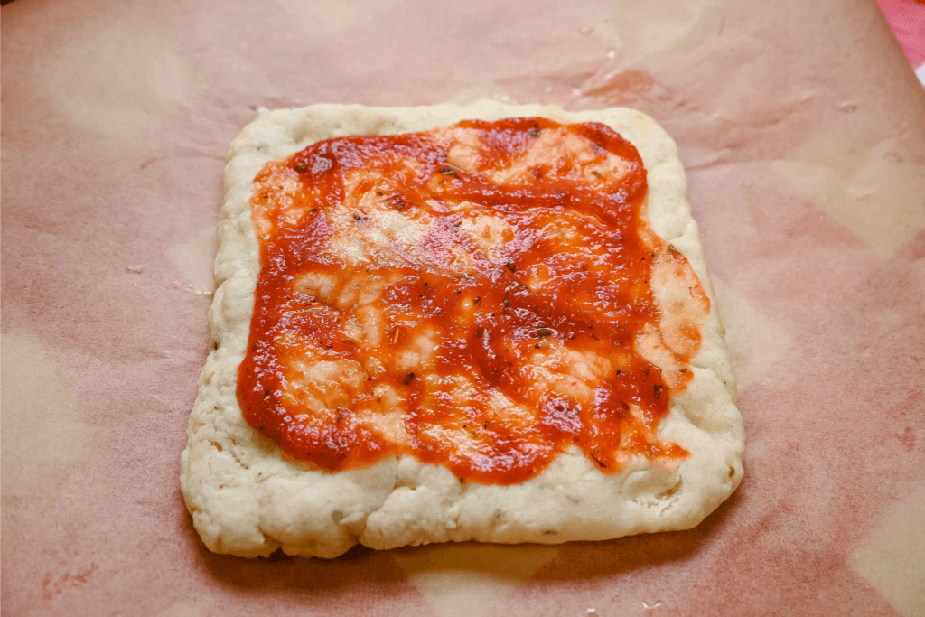 The pizza crust with sauce. 