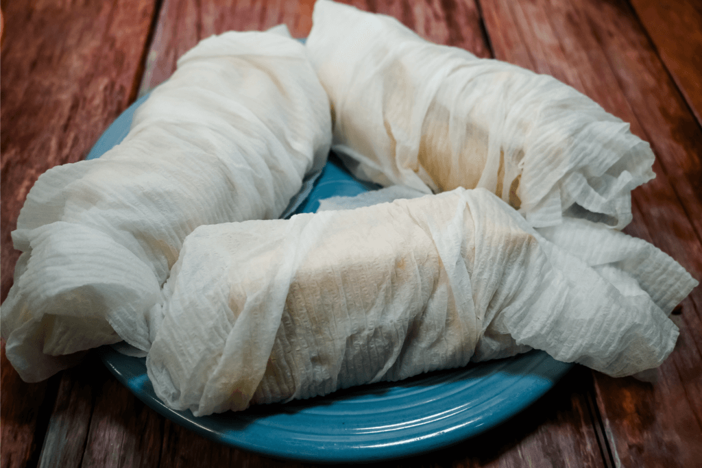 A blue plate with tamales wrapped in paper towels. 