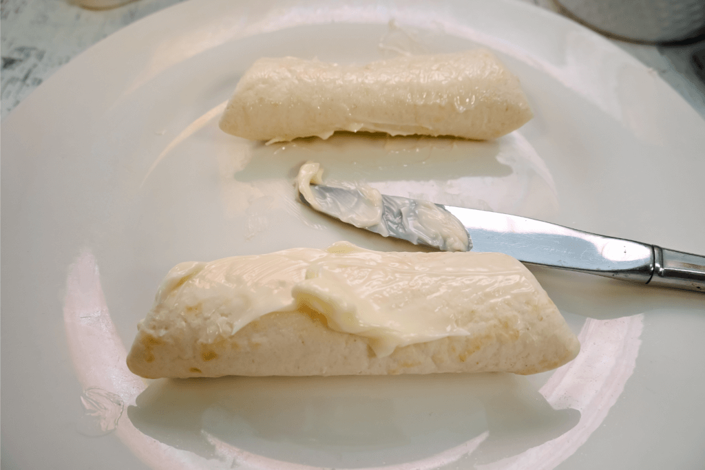 Butter being spread on the outside of each rolled up tortillas