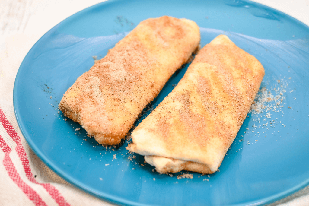 The finished microwave fried cheesecake chimichangas on a blue plate. 