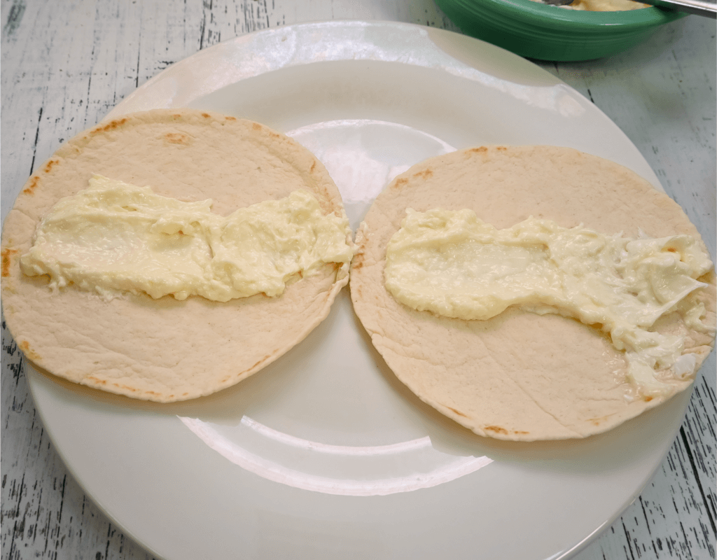 Two flour tortillas with cream cheese filling down the middle of each on a white plate. 