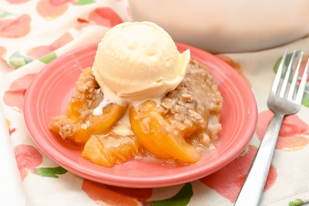 The peach crisp served on a coral saucer with a scoop of vanilla ice cream on top. 