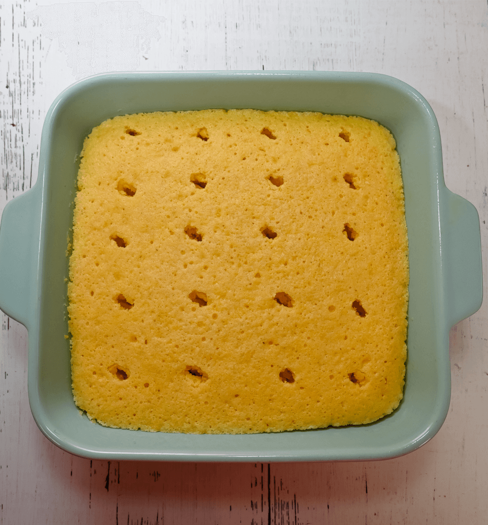 Light blue casserole dish with the cornbread with holes poked in it