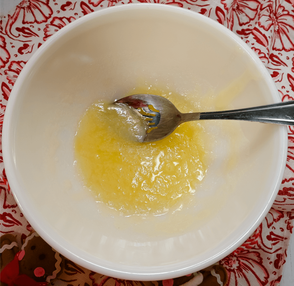 Melted butter mixed with white sugar in a glass bowl on a red floral towel