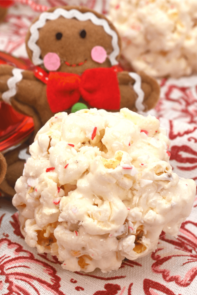 Close up of a finished peppermint popcorn ball in front of a gingerbread man. 