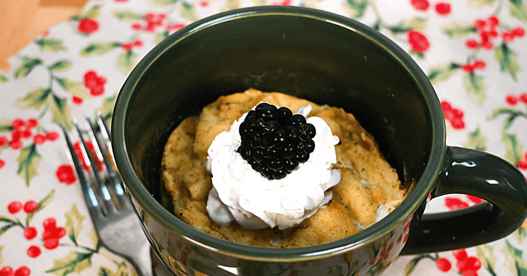 French Toast Casserole in a Green Mug topped with whipped cream and a blackberry on a floral placemat