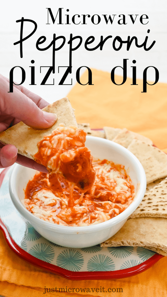 A white bowl on a red and blue plate filled with pepperoni pizza dip made in the microwave with slices of pita bread around it and a hand holding a slice of pita bread freshly dipped into the dip