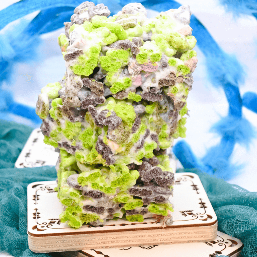 A stack of monster mash marshmallow treats on a wooden tarot card with a blue spider behind them