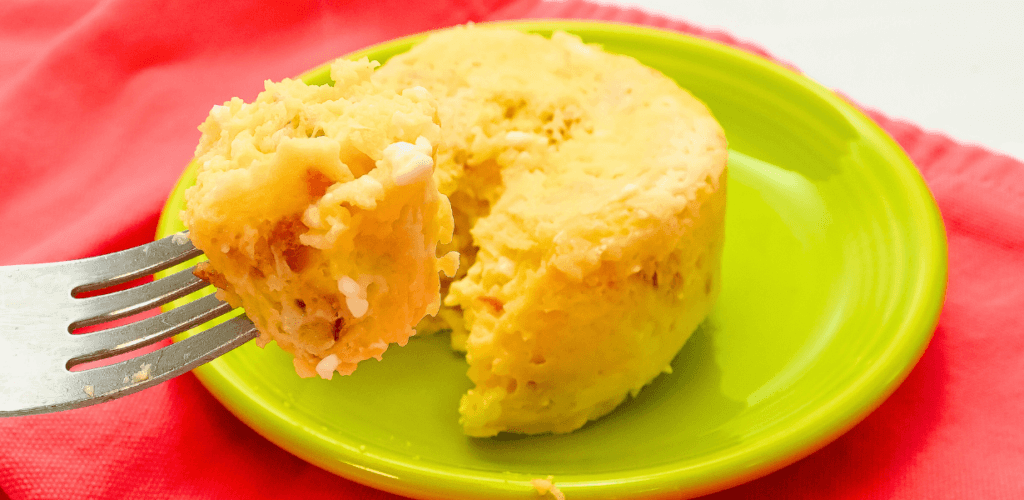 Close up of a green plate on a corral towel with a fork taking a bite from the single serving cheesy bacon egg casserole made in the microwave. 