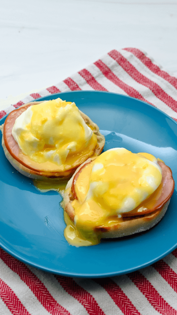 Eggs Benedict on a blue plate over a red-striped towel with microwave hollandaise sauce