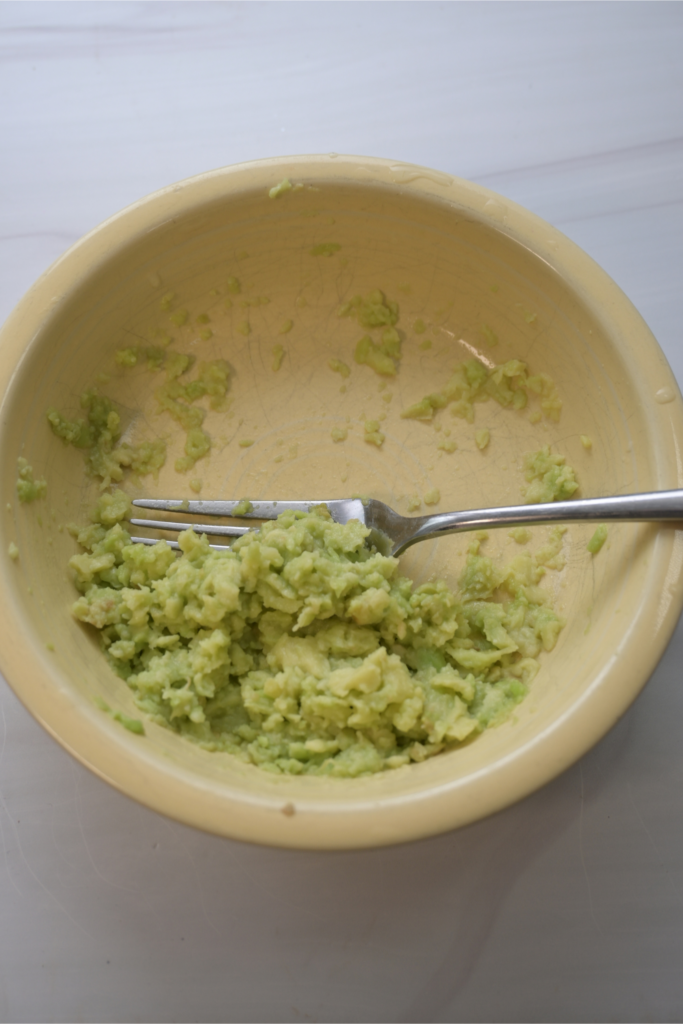 Close up of smashed avocado in a yellow bowl with a fork