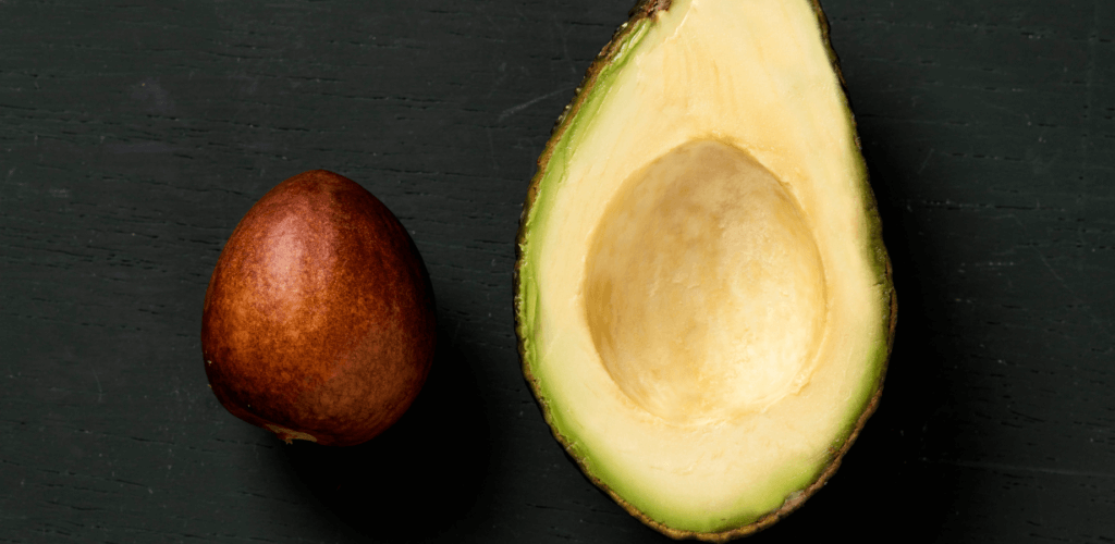 An avocado on a black surface with the pit removed