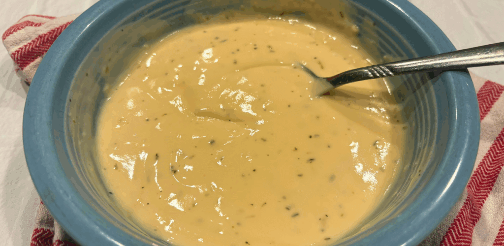 A blue bowl with homemade gluten free Alfredo sauce on a white and red striped towel 