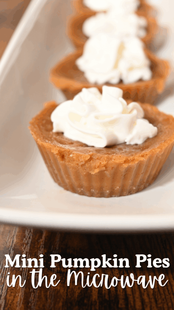 A line up of mini pumpkin pies freshly cooked in the microwave topped with whipped cream on a white platter on a brown wood table. 