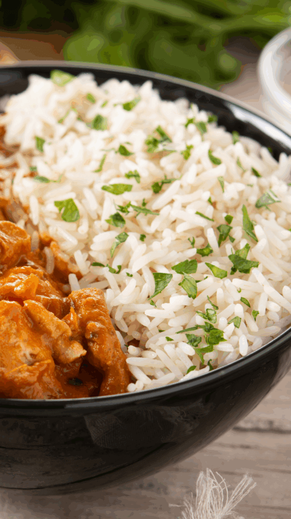 Close up of butter chicken with white rice in a black bowl