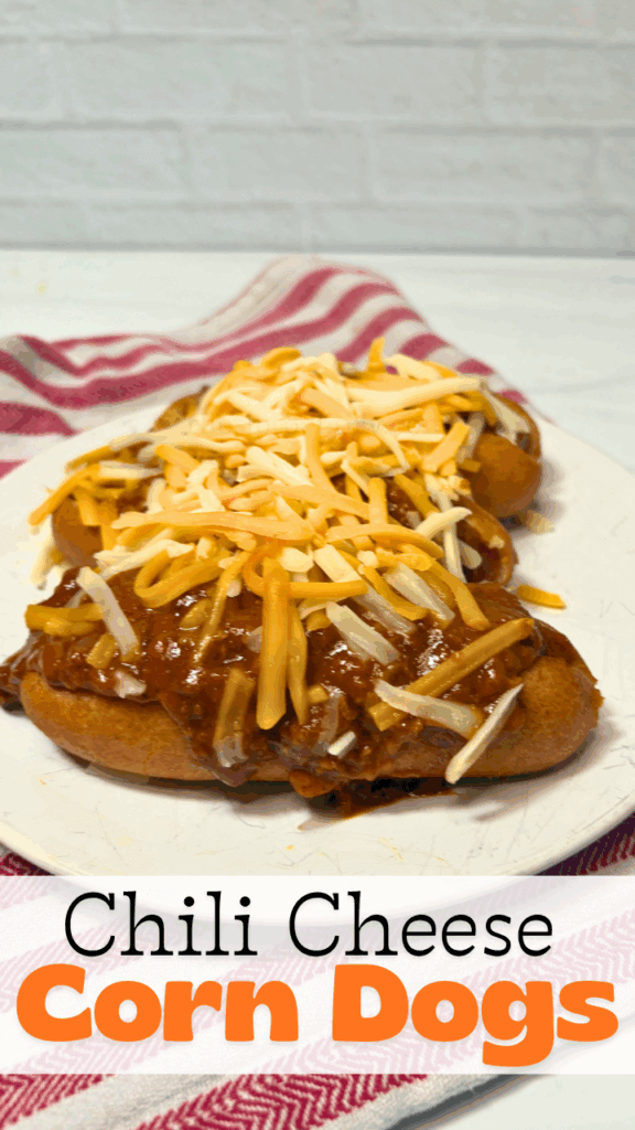 A close up of three chili cheese corn dogs on a white plate sitting on a white and red striped towel.