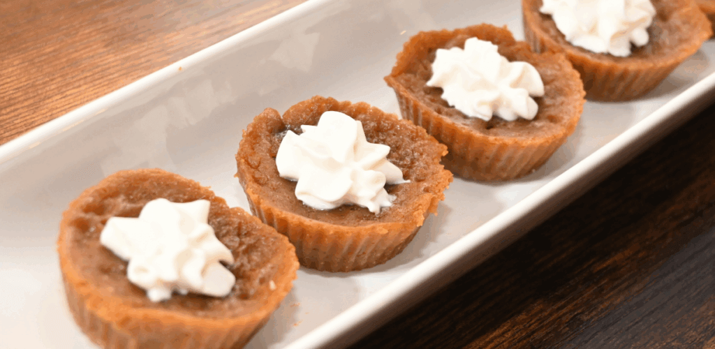 A set of four mini pumpkin pies I made in the microwave on a white platter on a wood grain table. 